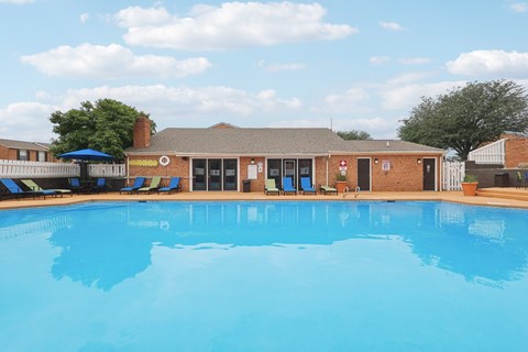 A large swimming pool in front of a building with a blue sky and clouds in the background.
