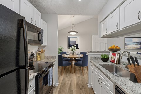A kitchen with a black refrigerator and a dining table with chairs.