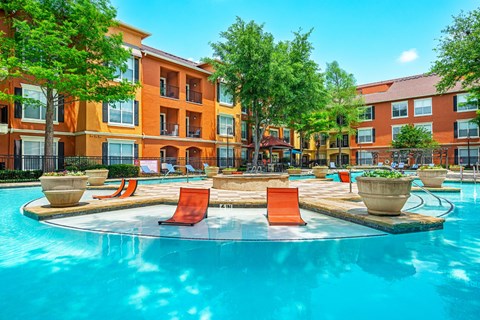 A swimming pool surrounded by orange chairs and potted plants in front of a multi-story apartment building.