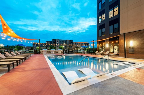A pool area with a long row of sun loungers and a building in the background.