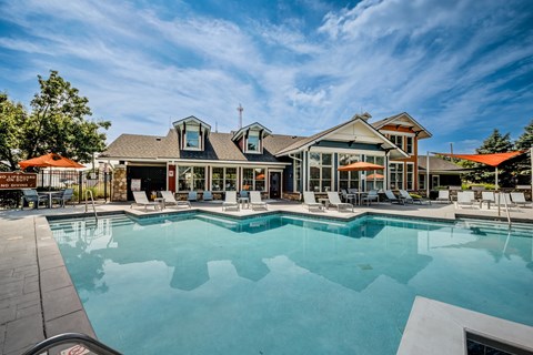 A large swimming pool in front of a building with a patio and lounge chairs.