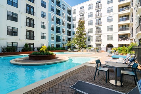 A pool surrounded by a patio with chairs and a table.