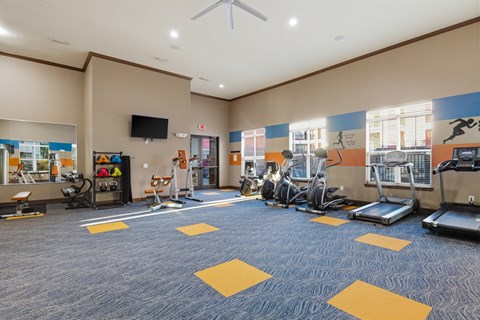 A gym with a variety of exercise equipment and a television.