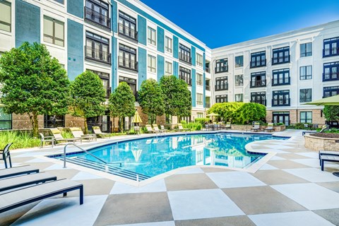 A large swimming pool surrounded by a tiled floor and lounge chairs.