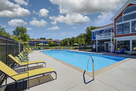 A swimming pool with yellow sun loungers and a building in the background.