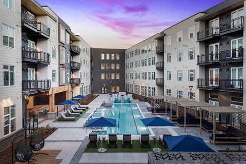 A swimming pool surrounded by lounge chairs and umbrellas in a residential area.