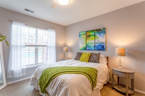 A bedroom with a bed, a nightstand, and a window with curtains.