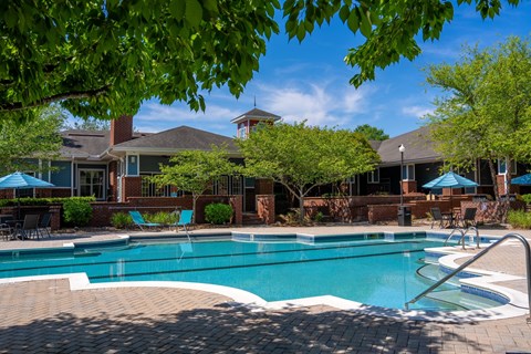 A swimming pool surrounded by a brick patio and a house with a red roof.
