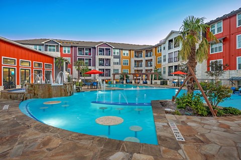 A pool surrounded by a stone patio and a building with red and orange walls.