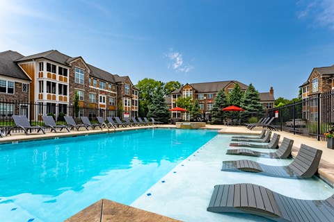 A large swimming pool surrounded by lounge chairs and umbrellas in front of a building.