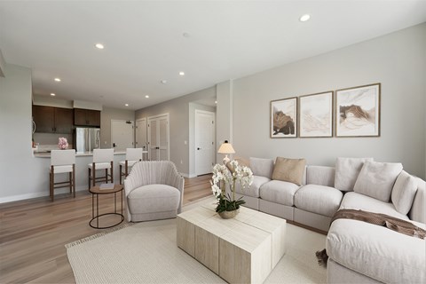 A living room with a white couch, a coffee table, and a dining area in the background.