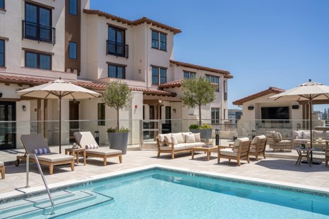 A pool area with chairs and umbrellas in front of a building.