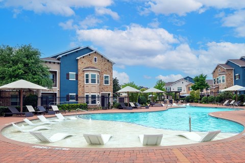 A swimming pool surrounded by lounge chairs and umbrellas in front of a building.