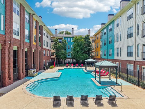 A pool with chairs and a gazebo in front of apartment buildings.