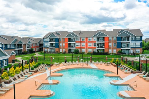 A large swimming pool surrounded by lounge chairs in front of apartment buildings.