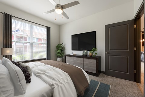 A bedroom with a bed, a ceiling fan, a television, and a window with blinds.