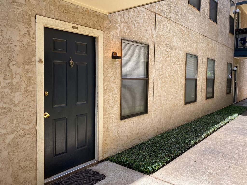 A black door is on the left side of a building with a wall that has a pattern.