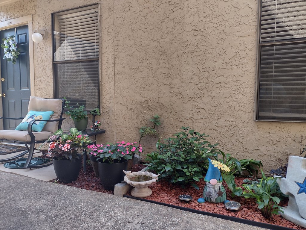 A small garden in front of a house with a blue chair and a wreath on the door.