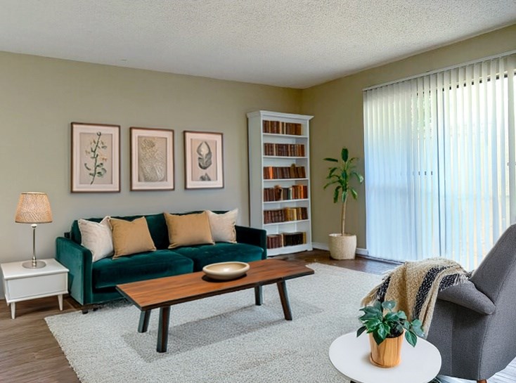 A living room with a green couch, a wooden coffee table, a white side table, a bookshelf, and a potted plant.