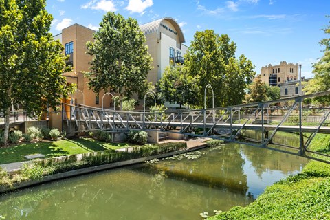 A bridge over a green waterway with trees and buildings in the background.