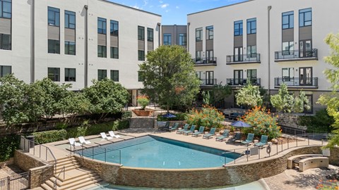 A swimming pool surrounded by chairs and trees in front of apartment buildings.