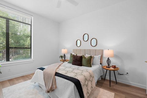A bedroom with a bed, a small table with a lamp, and a window with blinds.