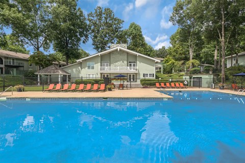 A swimming pool in front of a house with orange lounge chairs.