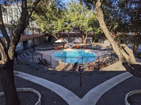 A pool surrounded by trees and a white fence.