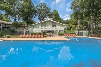 A swimming pool in front of a house with orange lounge chairs.