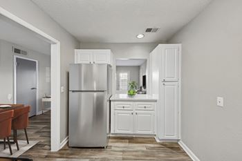 A kitchen with a refrigerator, cabinets, and a dining table.