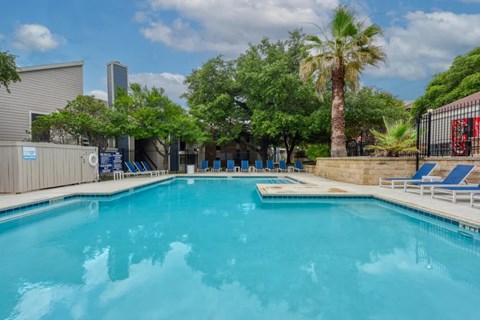 A large swimming pool surrounded by trees and lounge chairs.