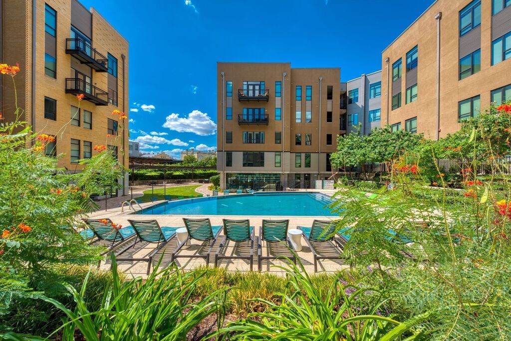 A pool surrounded by chairs and plants in front of apartment buildings.