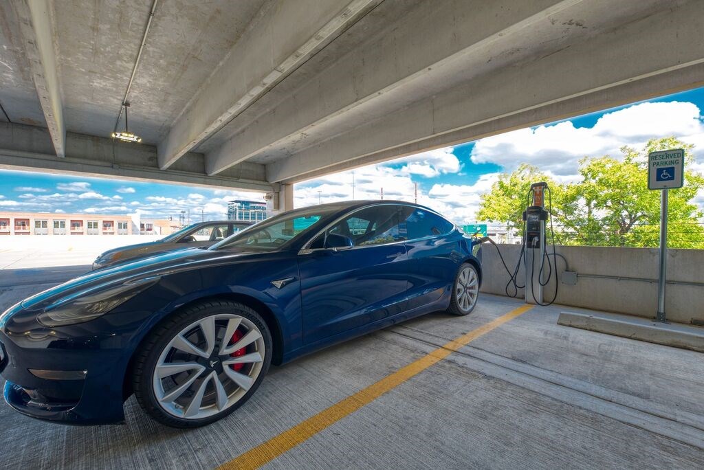 A blue Tesla car is parked and charging at a charging station.