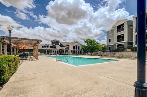 A large outdoor swimming pool surrounded by a concrete patio and buildings.