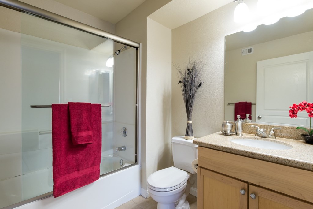 A red towel hangs on a glass shower door in a bathroom.
