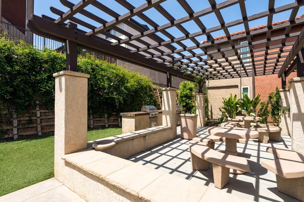 A patio with a wooden pergola and concrete furniture.