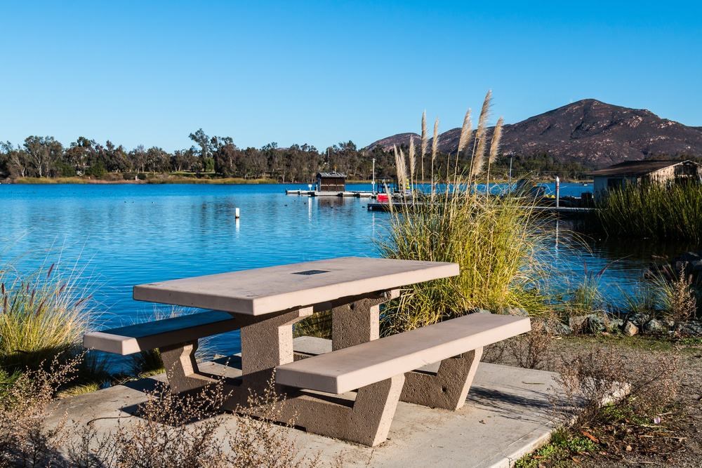 A picnic table sits in front of a lake with a mountain in the background.