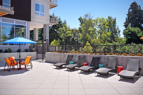 A patio with chairs and a table with a blue umbrella. at Kirkland Crossing Apartments, Kirkland, Washington