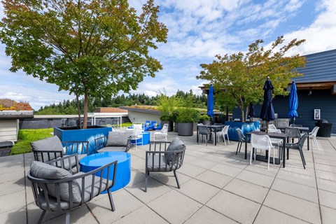 A patio with blue chairs and tables is surrounded by trees. at Kirkland Crossing Apartments, Kirkland, WA