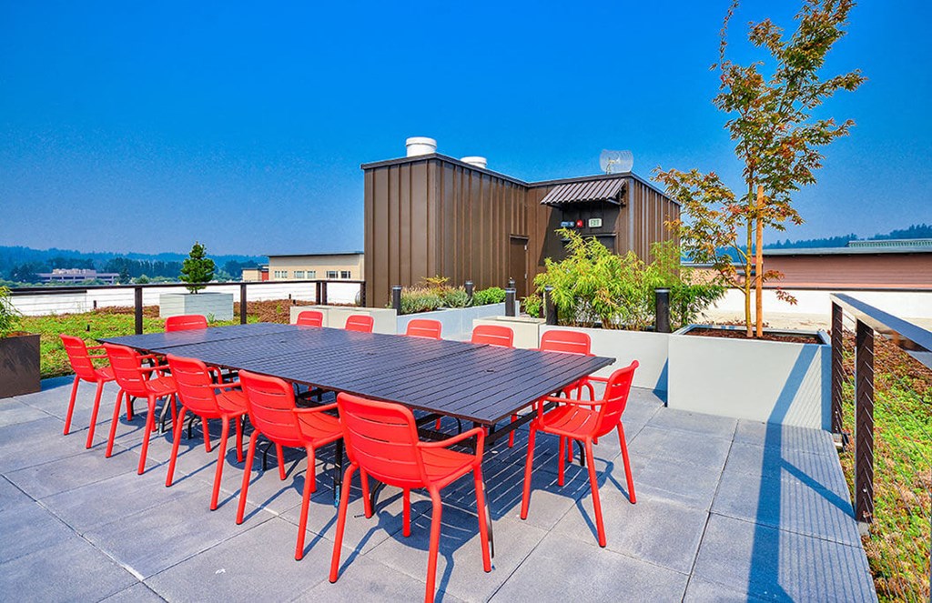 A table with red chairs is set up outside in front of a building. at Ravello Apartments, Redmond, WA