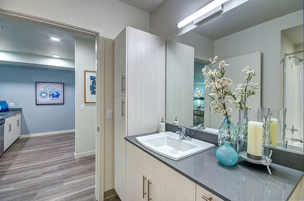 A bathroom with a sink, mirror, and a vase of flowers. at Ravello Apartments, Redmond, WA