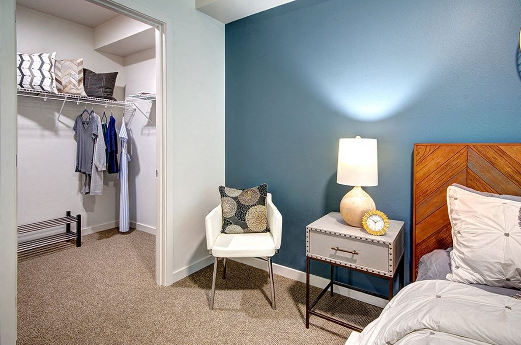 A bedroom with a bed, nightstand, chair, and closet. at Ravello Apartments, Redmond