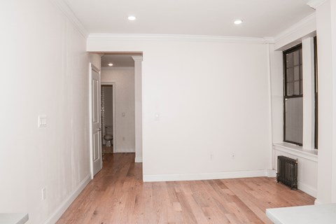 A white room with wood flooring and a window.