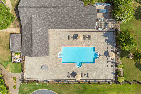 A large swimming pool surrounded by a stone patio and a grassy lawn.