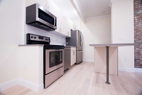 A kitchen with stainless steel appliances and a brick wall.