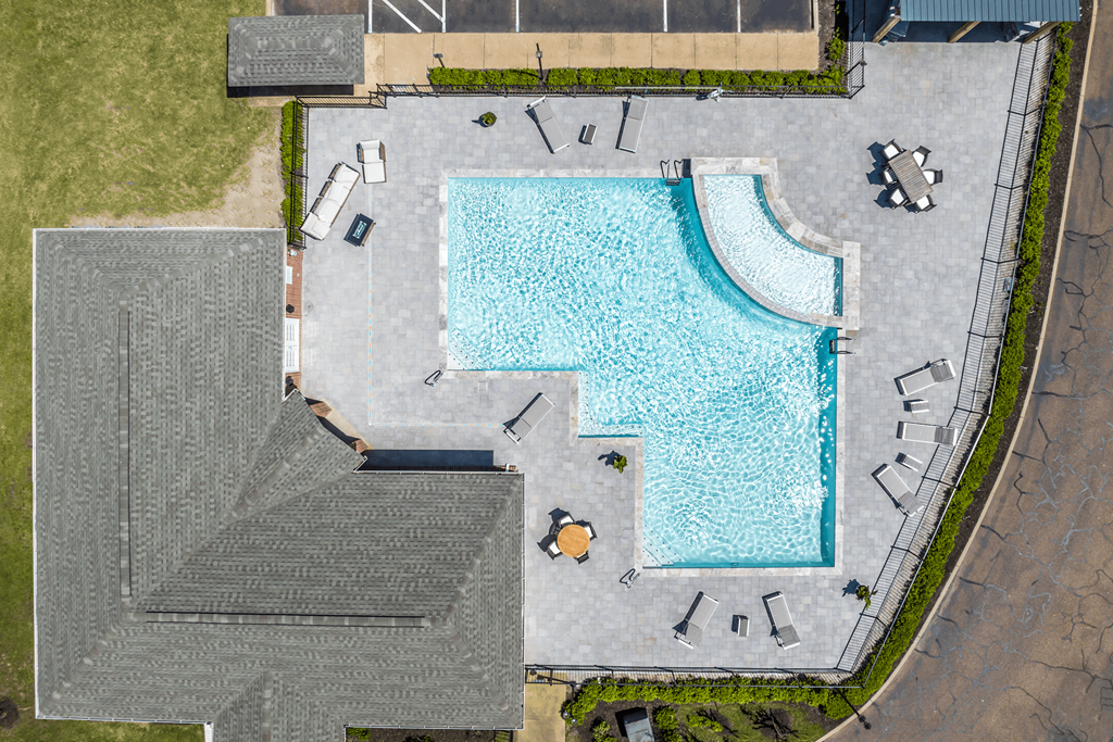 An aerial view of a swimming pool surrounded by a concrete patio and a grassy area.