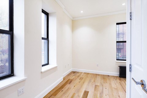 A room with a white door, a window with blinds, and a wooden floor.