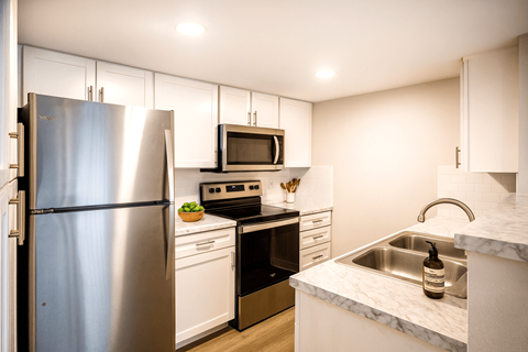 A kitchen with a stainless steel refrigerator, a microwave, a stove, and a sink.