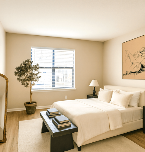 A bedroom with a bed, a potted tree, and a painting on the wall.