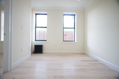 A room with two windows and a radiator on the floor.